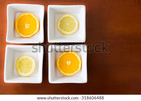 Slices of lemon and orange in white square bowls on wooden background