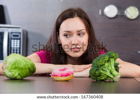 Young woman chooses what to eat vegetables or a cake