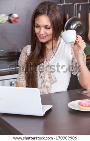 Young woman at home in the kitchen and looking at the computer