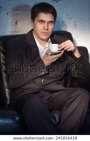 Young man in suit sitting on sofa and drink coffee