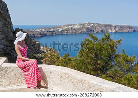 Woman n a long summer dress sits and watches the sea. Greece Santorini