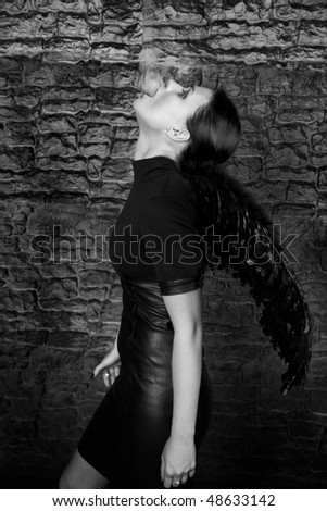 Beautiful woman with black wings smokes against a brick wall.