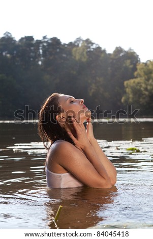 Beautiful young woman in a white mac swim in the river