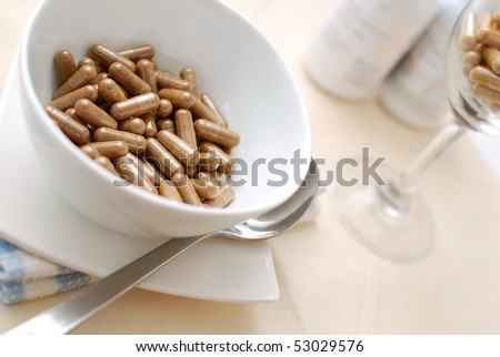 Medicine capsules in soup bowl with glass of capsules in background. Signifying drug addiction, healthy eating and lifestyle, dieting and slimming, and healthcare concepts.