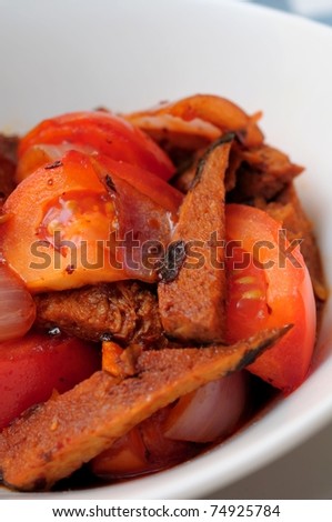 Macro shot of meat slices cooked with cut tomatoes.