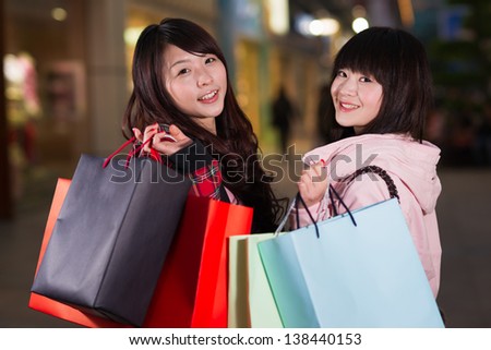 two happy chinese women with shopping bags in the business street at night