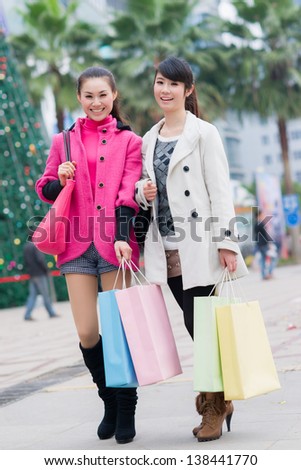 happy Chinese women with shopping bags in business street