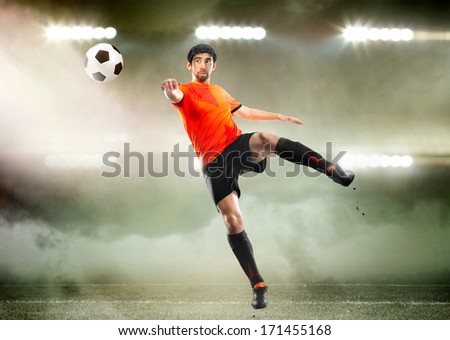 football player in orange shirt striking the ball at the stadium