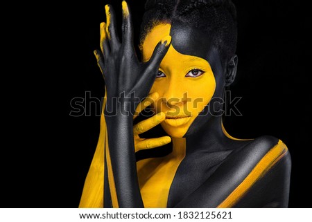 Face art. Woman with black and yellow body paint. Young african girl with colorful bodypaint. An amazing model with yellow makeup. Closeup face.
