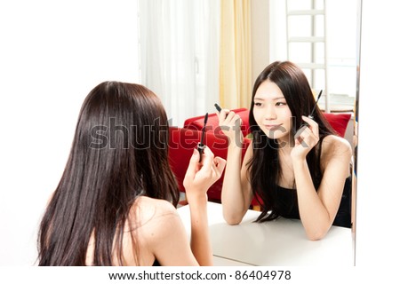attractive asian woman making up front of mirror