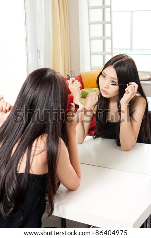 attractive asian woman making up front of mirror