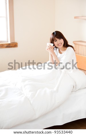 attractive asian woman drinking a cup of tea on the bed