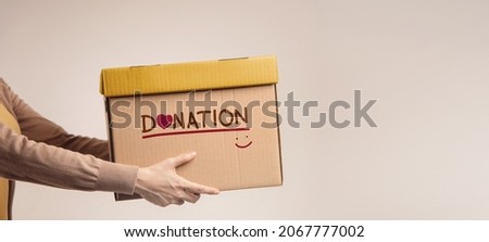 Donation Concept. Woman with Box of Things for Donate with Donation label, Smiling and Heart. Standing against the Walll. Side View Foto d'archivio © 