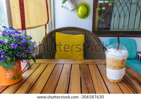 Ice cappuccino coffee in plastic glass, on the wood table in coffee shop. Natural light from window.