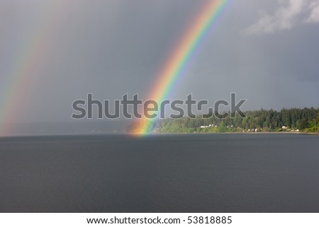 Brilliant rainbow over water and land. Bainbridge Island is seen accross Port Orchard Bay. Located in Kitsap County, Washington.