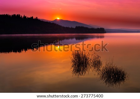 Beautiful sunset landscape with purple skies, mountain horizont line and silent lake