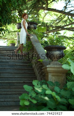 Beautiful young woman strolling through the old summer garden