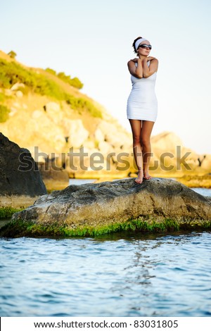 Beautiful woman standing on a stone in the sea and looking far away