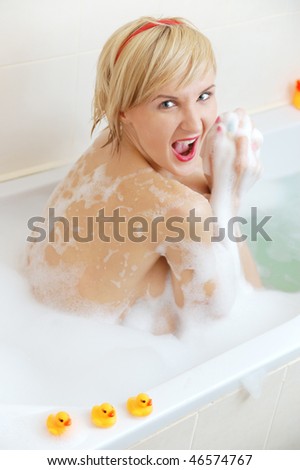 Angered blond woman lying in bubble bath with toy duck