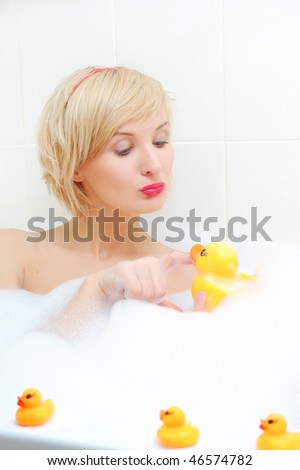Smiling blond woman lying in bubble bath with toy duck