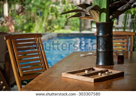 Board games on the wooden table in a tropical garden with swimming pool