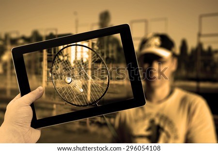 Photo tablet PC in hand with torn tennis badminton racket with stuck shuttlecock inside during play match