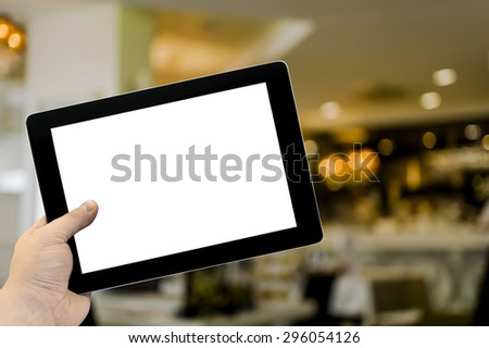 Empty tablet PC in hand in cafe bar interior with lamps