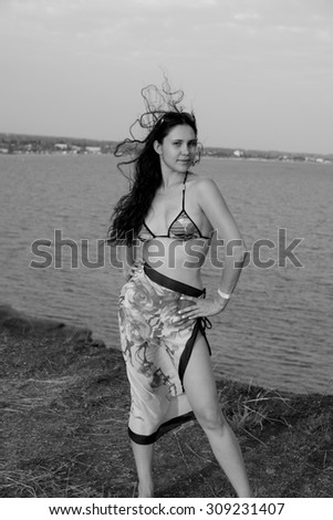 Young brunette girl in bikini and pareo on edge of mountain near sea black and white