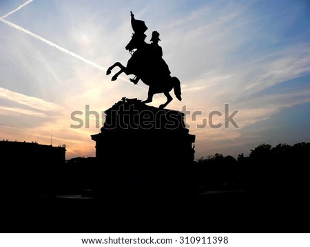 Black silhouette of monument of horse rider with flag on background of rose sunset