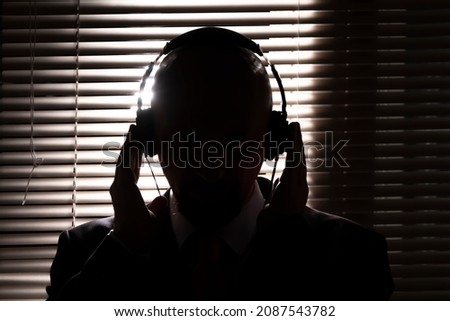 Silhouette of an FBI secret agent, listening with headphones and recording the conversation against the backdrop of a window with blinds, silhouette lighting, selective focus, dark tonality. Zdjęcia stock © 