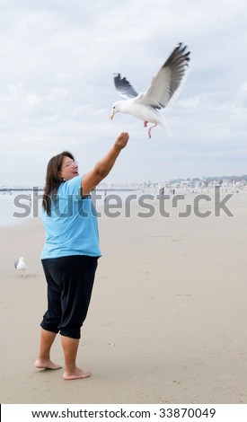 Lady at the beach feeding birds as they fly by and grab food midair
