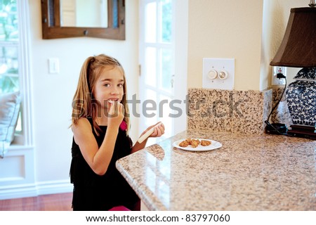 Little girl has a snack of cookies and string cheese in the kitchen after school