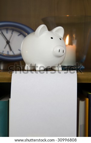 white piggy bank sitting on a book shelve with a white blank piece of paper to add your own text,