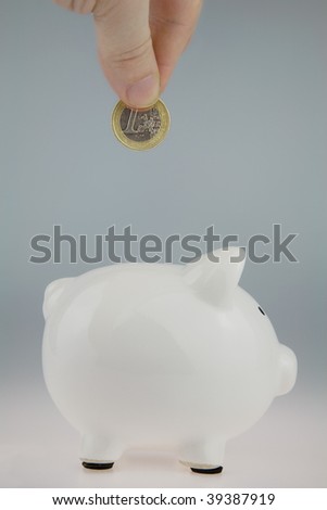 White Piggy Bank with a persons Hand above about to drop a One Euro Coin into the slot,