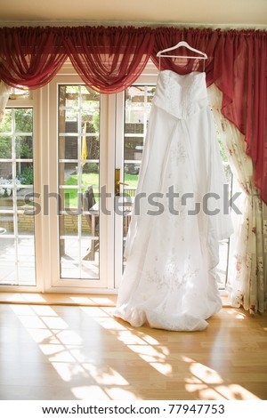 white Wedding dress hanging from a curtain pole with the sun shining through the window,