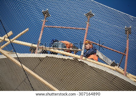 PODOLSK, 28.04.2015 - workers on the eage of the building behind the mesh