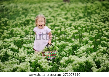 Little girl stands in a meadow with a basket of flowers and laughing