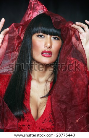 Beautiful east woman in a red dress lifts over the face a veil, isolated on a black background