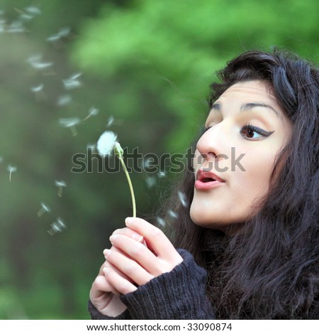 Summer fun, young beautiful woman with magnificent hair, blowing dandelion on the meadow