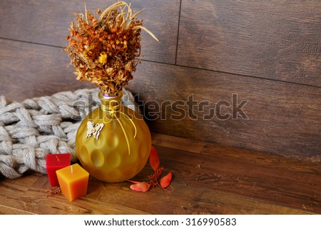 Vase with dried flowers, candles and knitted warm scarf on wooden table. Winter and autumn vintage background.