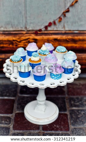 Mini cupcakes on a wooden white stand. Dessert in autumn decoration with dry yellow leaves. Natural light