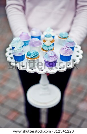 Hands holding mini cupcakes on a wooden white stand. Natural light
