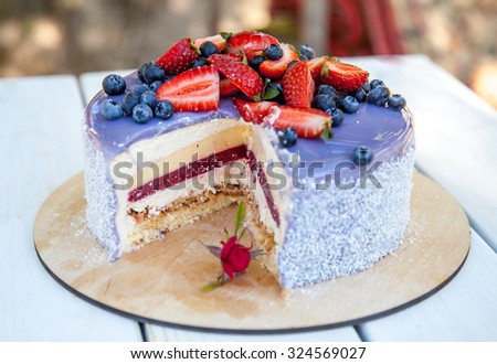 Delicious sliced cake. Glazed with chocolate mirror lavender glaze, decorated with strawberries and blueberries. Natural light