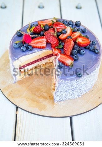 Delicious sliced cake. Glazed with chocolate mirror lavender glaze, decorated with strawberries and blueberries. Natural light
