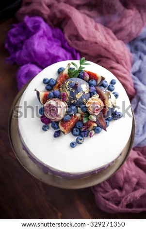 Perfect cake decorated with blueberries, figs, dry roses, edible gold and dry sugar violas. Stylized with cheesecloth. Natural light.