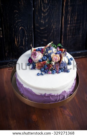 Perfect cake decorated with blueberries, figs, dry roses, edible gold and dry sugar violas. Natural light.