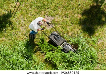The man takes care of the lawn. Top view. A man mows the lawn with a lawn mower