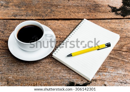 Black coffee in white cup with note book and yellow pen on wood background.