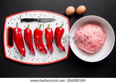 In the kitchen whiteboard red peppers in a row near the bowl with minced chicken, eggs, pepper to peas on a black background. Red peppers and minced chicken. Top view. Horizontal shot.