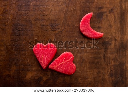 On the left side of the frame 2 hearts of watermelon flesh in the upper right the moon on a wooden background. 2 Watermelon hearts and moon. Top view. Close-up. Daylight. Horizontal shot.